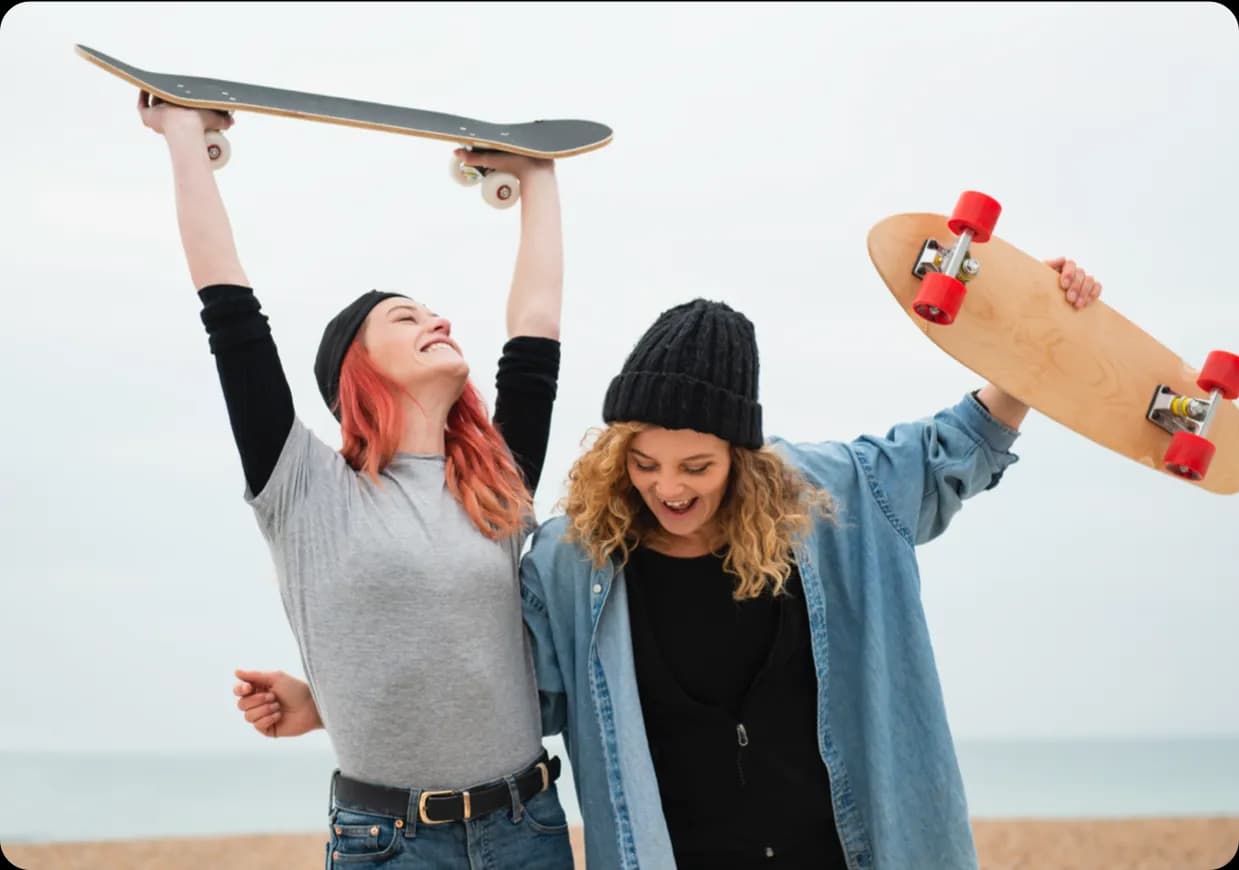 Two women smiling and holding up skateboards.