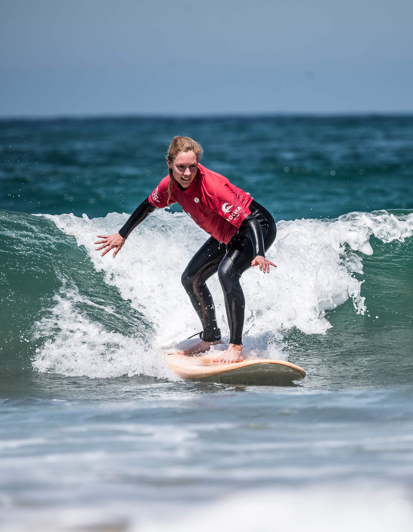 A happy young woman with a bright smile, riding her surfboard on a sunny day at the beach.