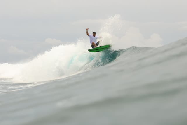 Man on a green surf board riding a wave.