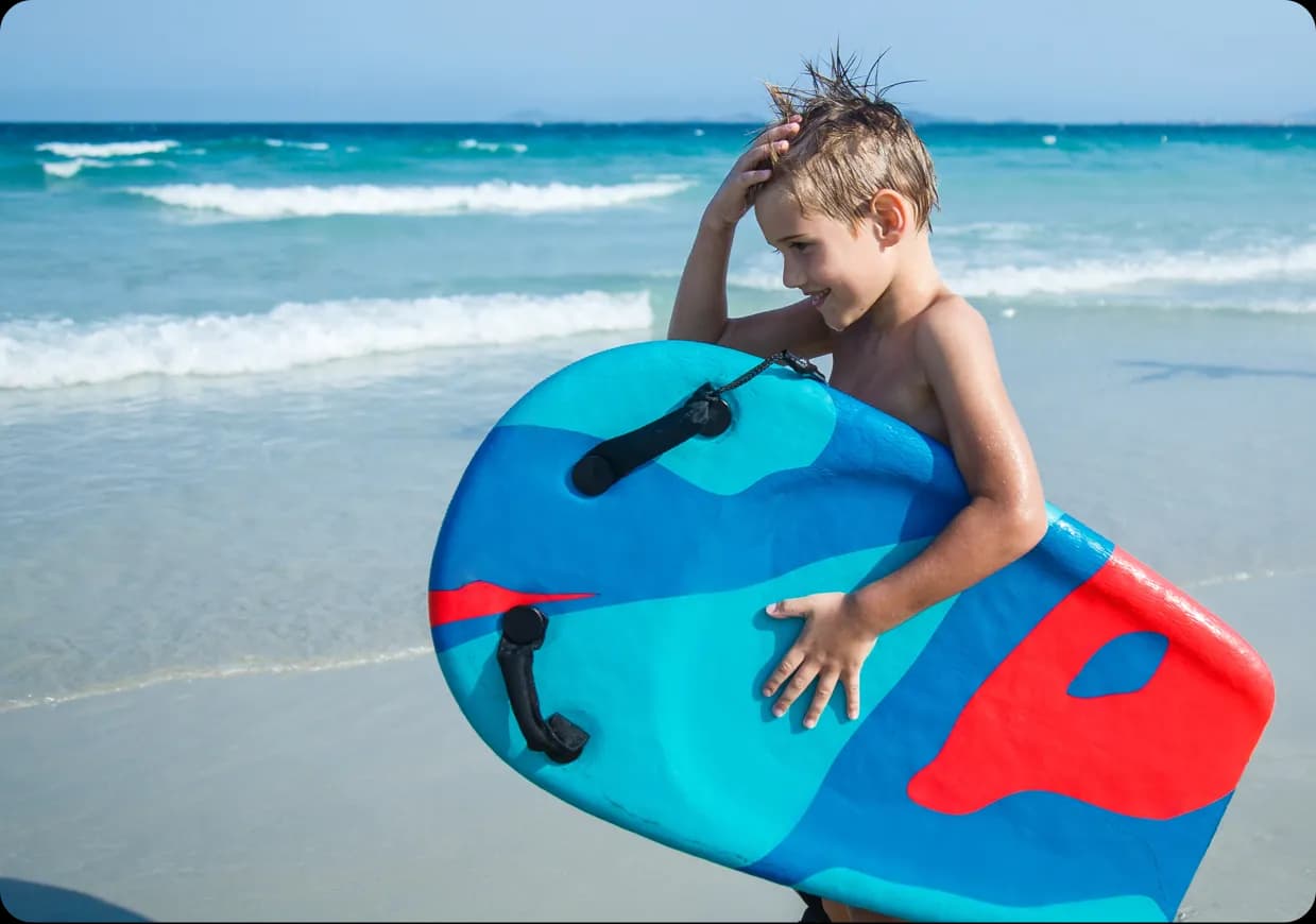 A kid holding a bodyboard ans smiling.