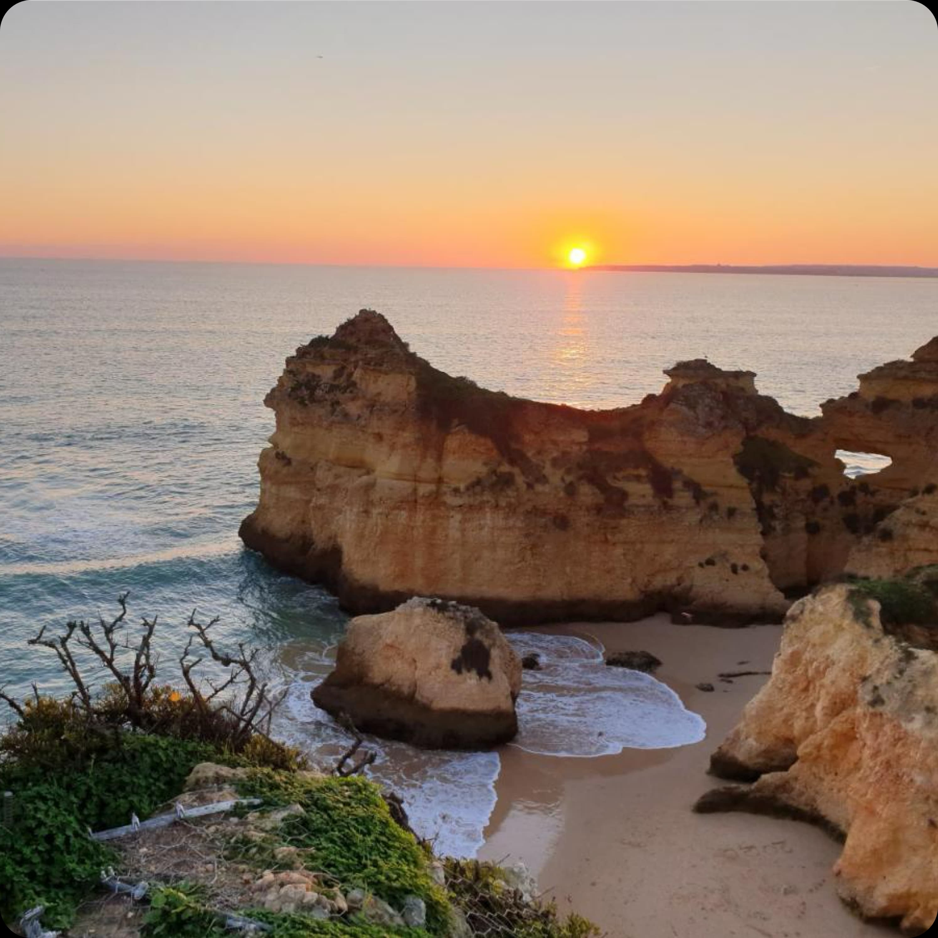 A stunning sunrise over a quiet Algarve beach, with golden light hitting the iconic rock formations.